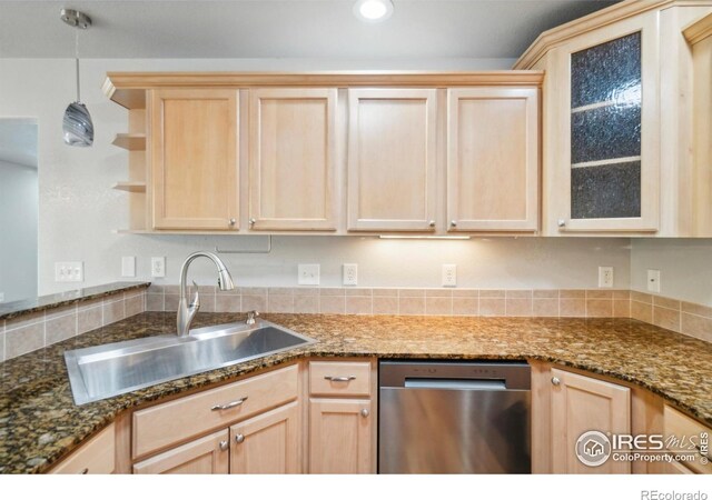 kitchen with dark stone counters, hanging light fixtures, sink, stainless steel dishwasher, and light brown cabinetry