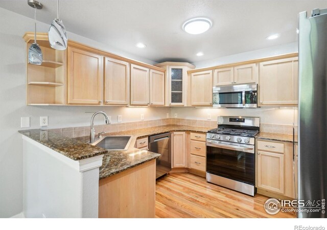 kitchen featuring kitchen peninsula, appliances with stainless steel finishes, dark stone counters, sink, and light hardwood / wood-style floors