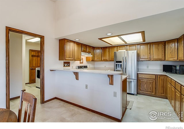 kitchen featuring a kitchen bar, kitchen peninsula, stainless steel appliances, and washer / clothes dryer