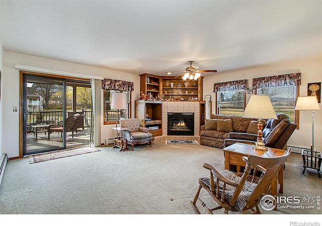 carpeted living room with ceiling fan, a tile fireplace, baseboard heating, and a wealth of natural light