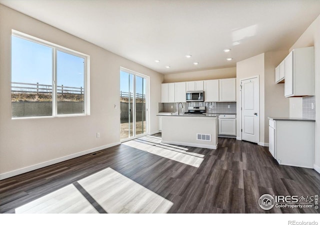 kitchen with white cabinets, stainless steel appliances, dark hardwood / wood-style floors, and an island with sink