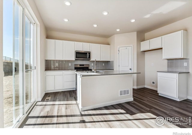 kitchen with hardwood / wood-style flooring, white cabinets, a center island with sink, and appliances with stainless steel finishes