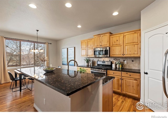 kitchen with an island with sink, an inviting chandelier, appliances with stainless steel finishes, and hanging light fixtures