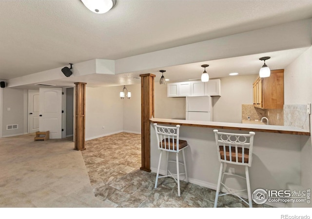 kitchen with white fridge, kitchen peninsula, a breakfast bar, white cabinets, and backsplash