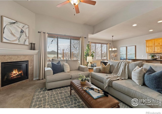 carpeted living room featuring ceiling fan with notable chandelier and a tiled fireplace