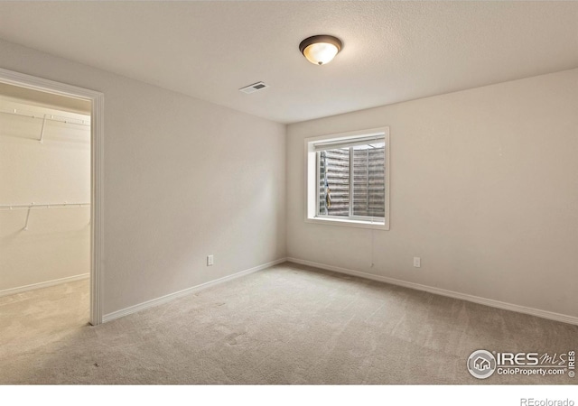 unfurnished bedroom with a walk in closet, a closet, and light carpet