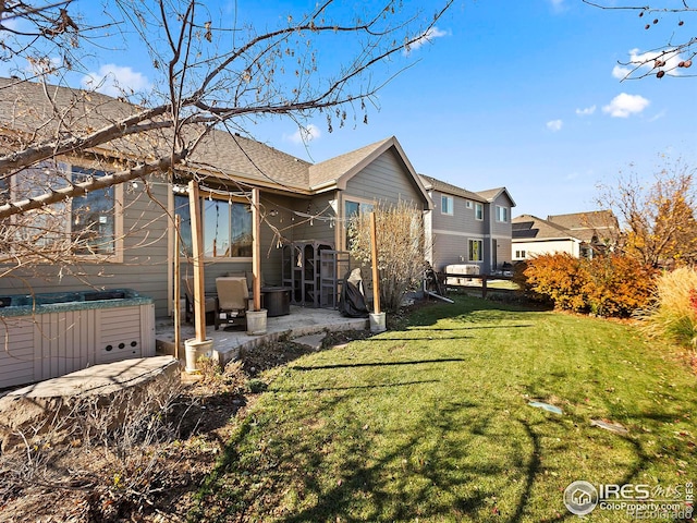 rear view of house featuring a patio area, a yard, and a hot tub