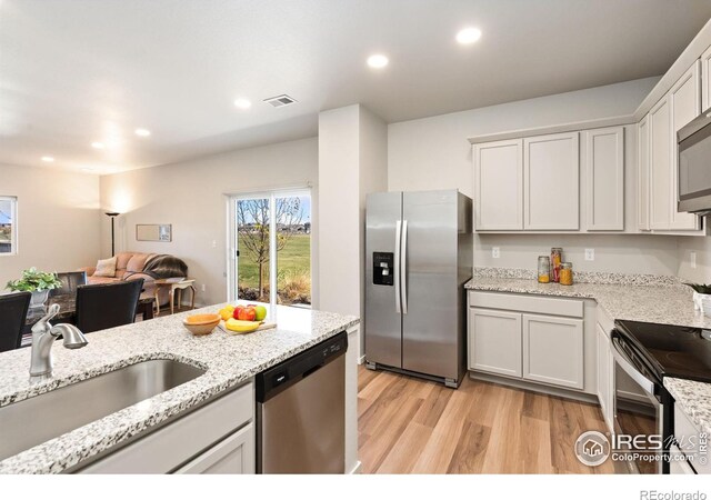 kitchen featuring appliances with stainless steel finishes, light stone counters, sink, light hardwood / wood-style floors, and white cabinetry