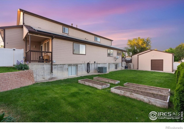 back house at dusk with a yard, a garage, cooling unit, and an outdoor structure