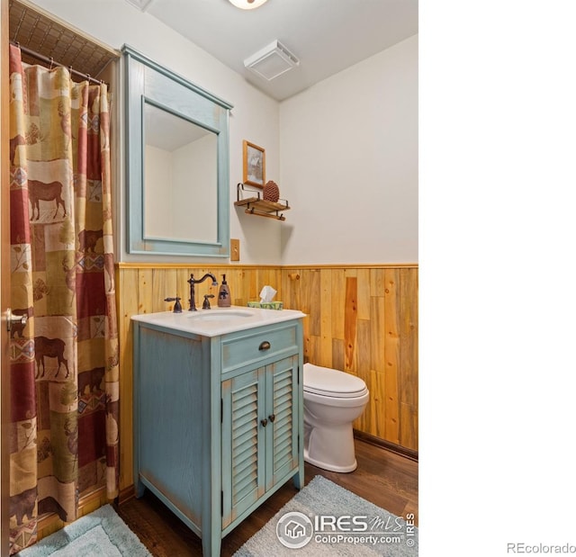 bathroom with hardwood / wood-style flooring, vanity, wood walls, and toilet