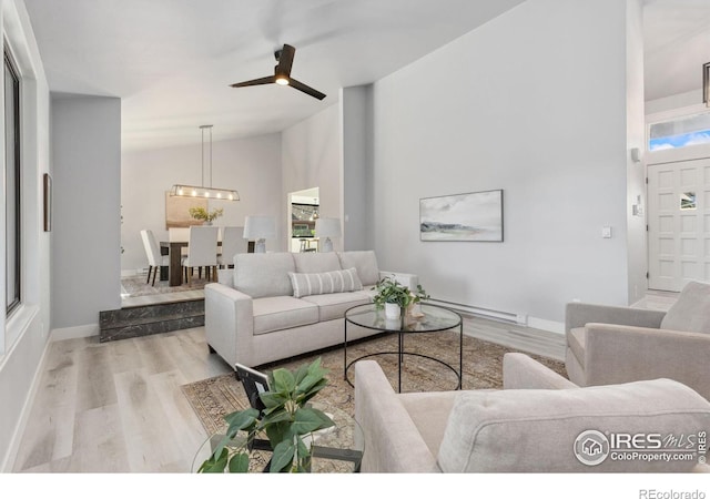 living room with light hardwood / wood-style flooring, high vaulted ceiling, a baseboard radiator, and ceiling fan with notable chandelier