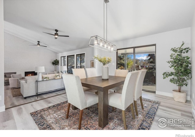 dining space featuring ceiling fan, light wood-type flooring, lofted ceiling, and a fireplace