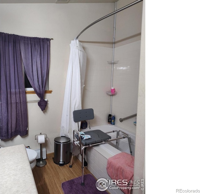 interior space with hardwood / wood-style floors, toilet, and shower / bathtub combination with curtain