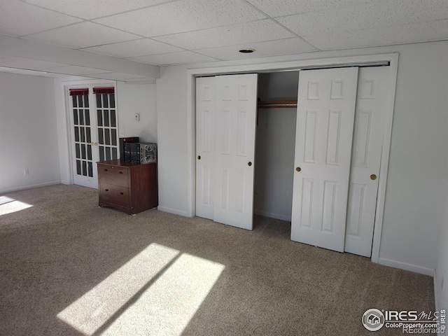 unfurnished bedroom with carpet flooring, a drop ceiling, and a closet