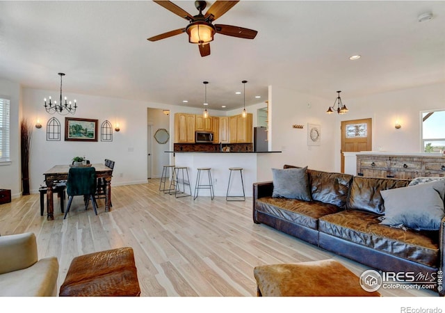 living room featuring ceiling fan with notable chandelier and light hardwood / wood-style flooring