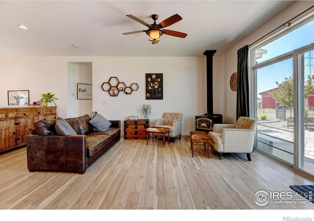 living room featuring ceiling fan, a wood stove, and light hardwood / wood-style flooring