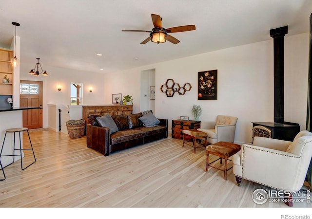 living room featuring ceiling fan with notable chandelier, a wood stove, and light hardwood / wood-style flooring