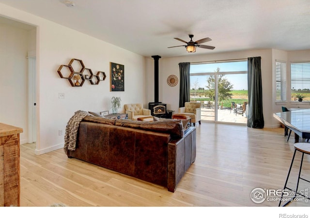 living room featuring ceiling fan, a wood stove, and light hardwood / wood-style floors