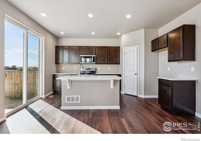 kitchen with sink, appliances with stainless steel finishes, dark hardwood / wood-style flooring, and an island with sink