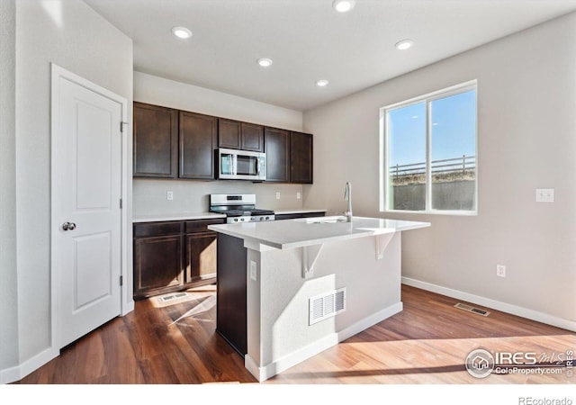 kitchen with a kitchen island with sink, wood-type flooring, sink, gas stove, and dark brown cabinetry