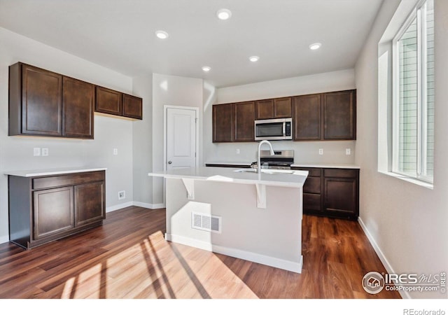 kitchen with a kitchen island with sink, dark hardwood / wood-style flooring, sink, and appliances with stainless steel finishes