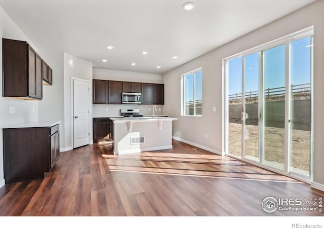 kitchen with dark wood-type flooring, a kitchen island with sink, white range, sink, and dark brown cabinets