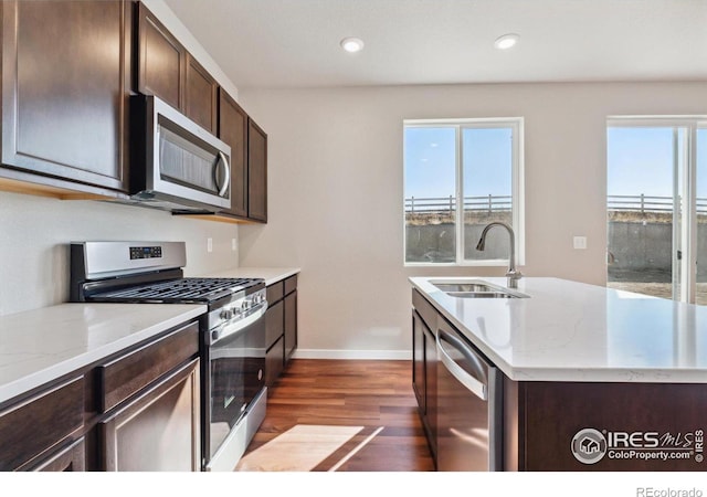 kitchen with appliances with stainless steel finishes, dark hardwood / wood-style flooring, dark brown cabinetry, sink, and an island with sink