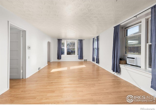 unfurnished living room with a textured ceiling, light hardwood / wood-style flooring, cooling unit, and a healthy amount of sunlight