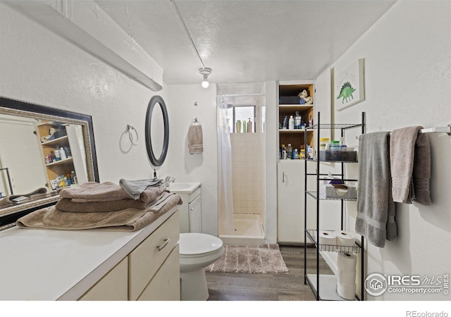 bathroom featuring a textured ceiling, tiled shower, toilet, vanity, and hardwood / wood-style flooring