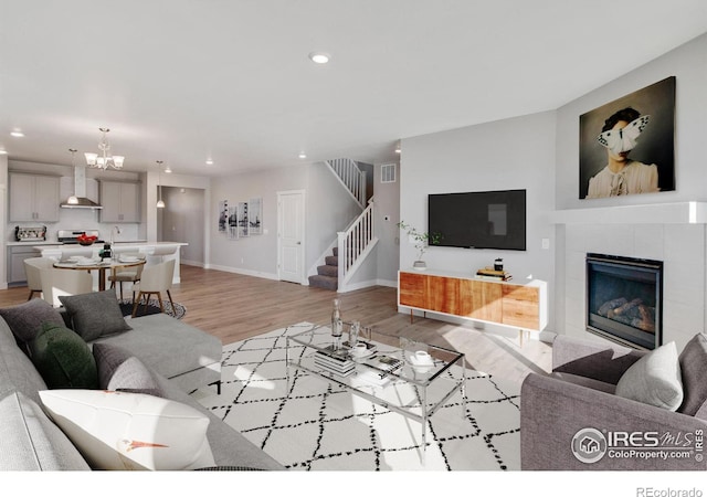 living room featuring a notable chandelier, light wood-type flooring, and a tile fireplace