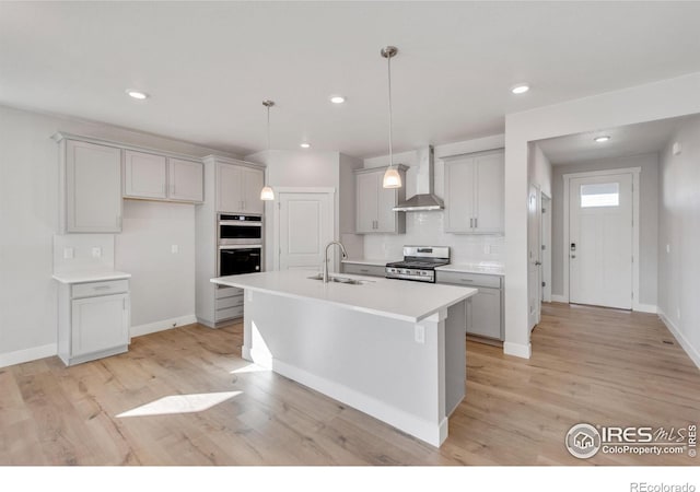 1815 Chaffee Crest Dr, Berthoud, CO 80513 - kitchen with sink, wall chimney range hood, light hardwood / wood-style flooring, a kitchen island with sink, and appliances with stainless steel finishes