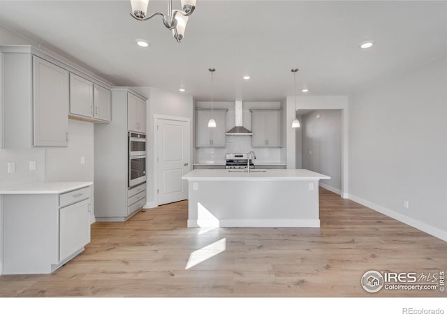 1815 Chaffee Crest Dr, Berthoud, CO 80513 - kitchen featuring a kitchen island with sink, wall chimney exhaust hood, decorative light fixtures, and light wood-type flooring