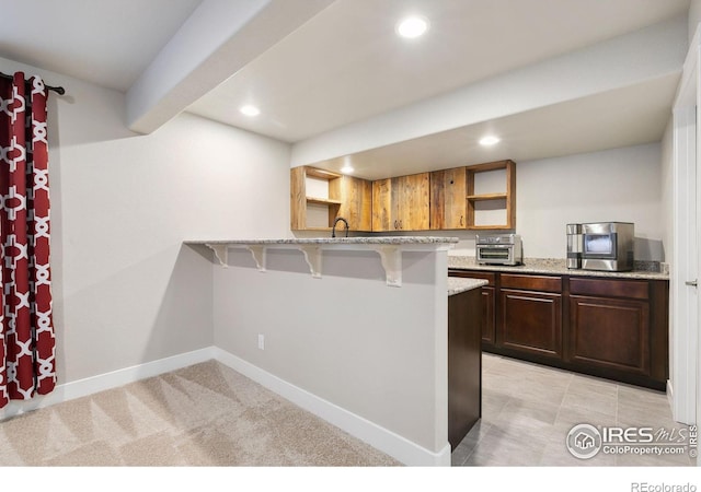 kitchen featuring sink, light stone counters, kitchen peninsula, light carpet, and a breakfast bar