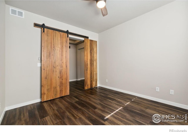 unfurnished bedroom featuring a barn door, ceiling fan, and dark wood-type flooring