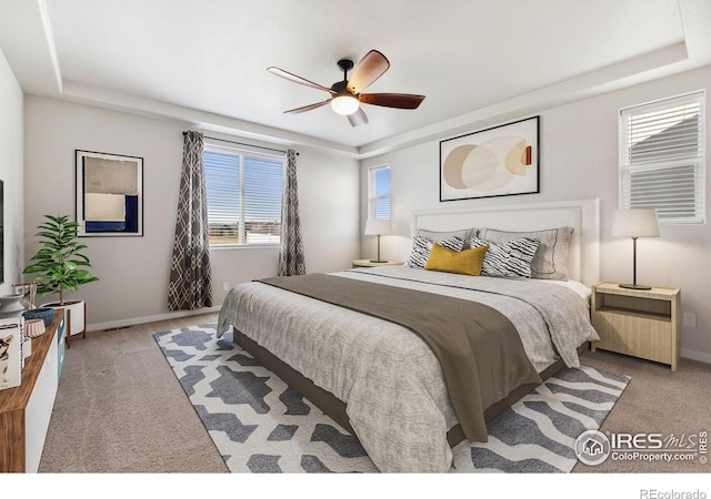 carpeted bedroom featuring a raised ceiling, a ceiling fan, and baseboards