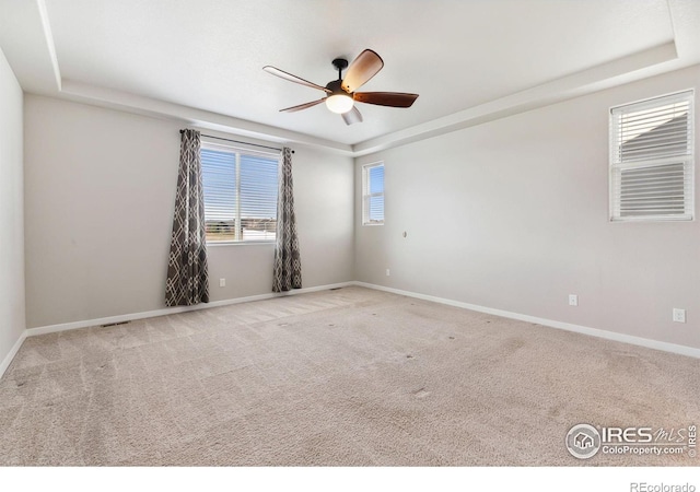 spare room with carpet floors, a raised ceiling, ceiling fan, and baseboards