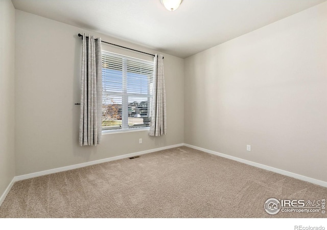 empty room with carpet, visible vents, and baseboards