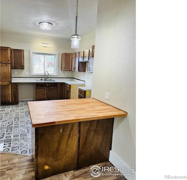 kitchen with kitchen peninsula, light wood-type flooring, sink, pendant lighting, and butcher block counters