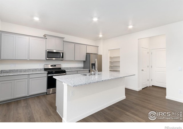 kitchen featuring stainless steel appliances, light stone counters, dark hardwood / wood-style flooring, gray cabinets, and a kitchen island with sink