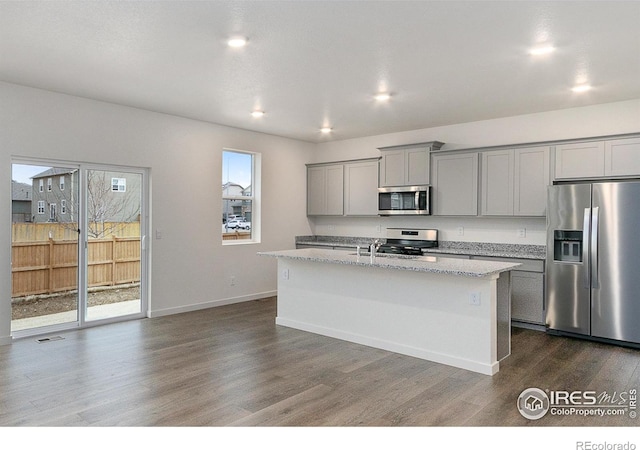 kitchen featuring light stone counters, gray cabinetry, stainless steel appliances, a center island with sink, and dark hardwood / wood-style floors