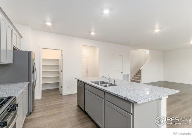 kitchen featuring gray cabinetry, sink, stainless steel appliances, light hardwood / wood-style floors, and a kitchen island with sink