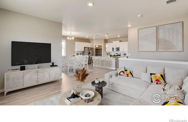 living room with sink, light hardwood / wood-style floors, and an inviting chandelier