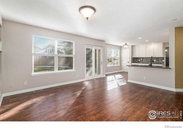 unfurnished living room with sink, a healthy amount of sunlight, and dark hardwood / wood-style floors