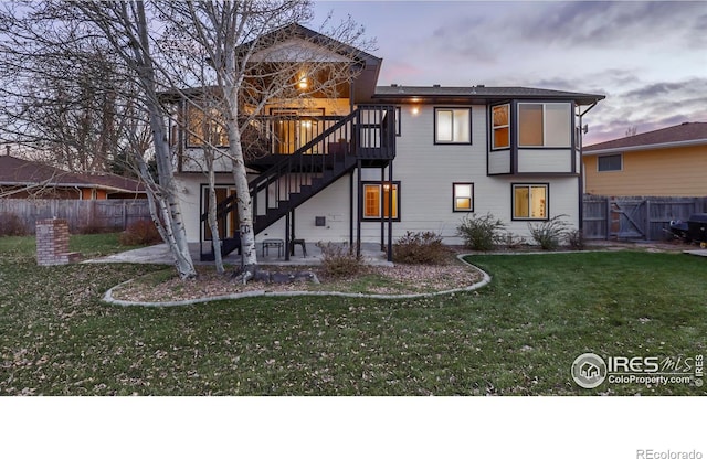 back house at dusk with a lawn, a patio, and a wooden deck