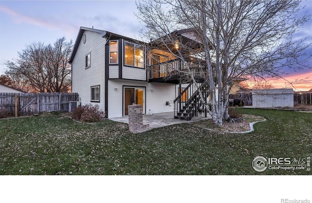 back house at dusk featuring a lawn, a storage shed, a patio, and a wooden deck