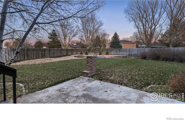 yard at dusk featuring a trampoline and a patio area