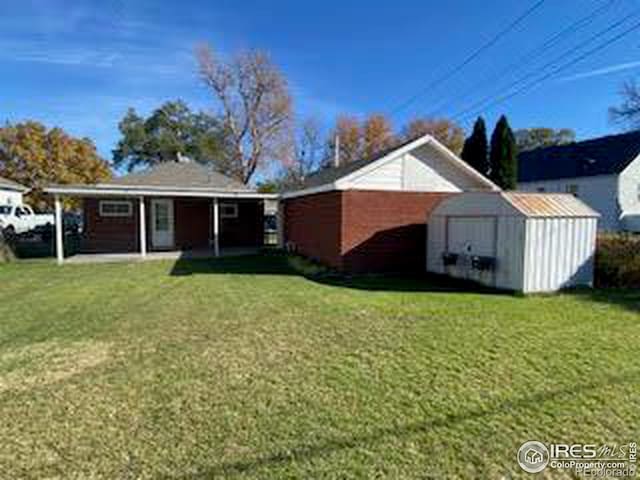 back of house with a lawn and a storage unit