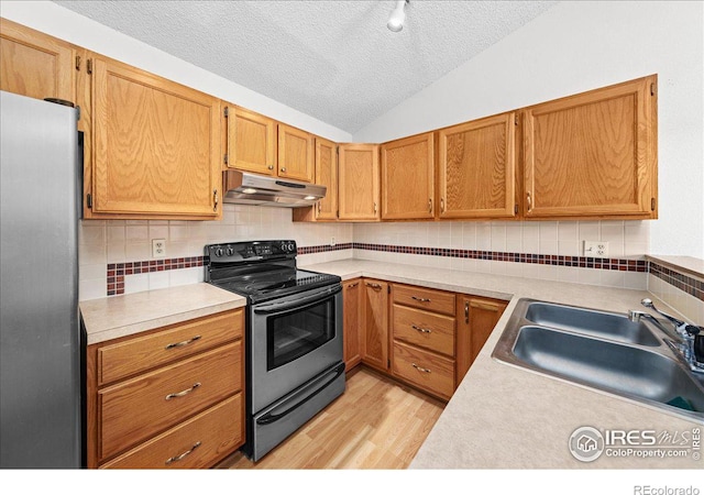 kitchen featuring vaulted ceiling, stainless steel appliances, light countertops, under cabinet range hood, and a sink