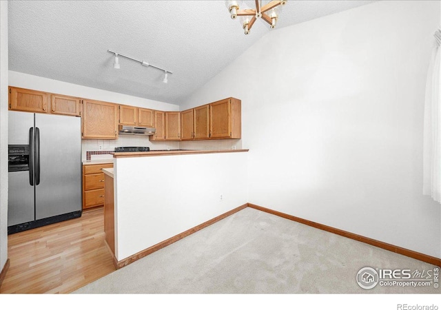 kitchen with vaulted ceiling, light countertops, a textured ceiling, under cabinet range hood, and stainless steel refrigerator with ice dispenser