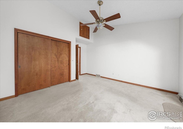 unfurnished bedroom with high vaulted ceiling, light colored carpet, visible vents, baseboards, and a closet